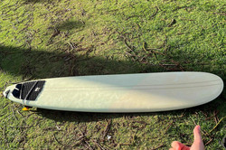 Surfboard Es zeigt ein Surfboard auf einer Wiese, rechts unten ist Will seine Hand abgebildet
