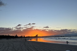 Blick auf einen orangenen Sonnenuntergang am Strand - mit Surfbrett in der Hand