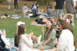 A group of participants are chatting on a picnic blanket in the park.