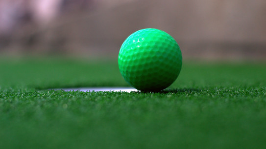 A green miniature golf ball near a hole on artificial turf.