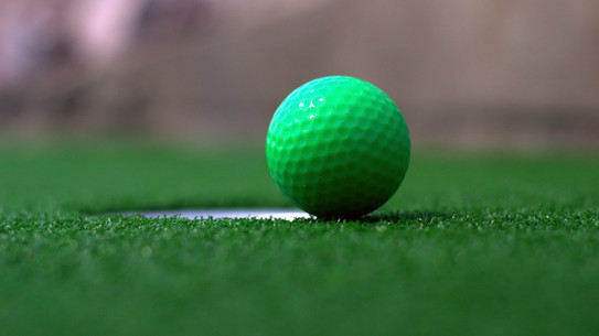 Ein grüner Minigolfball an einem Loch auf Kunstrasen.