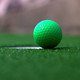 A green miniature golf ball near a hole on artificial turf.