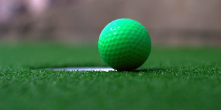 A green miniature golf ball near a hole on artificial turf.
