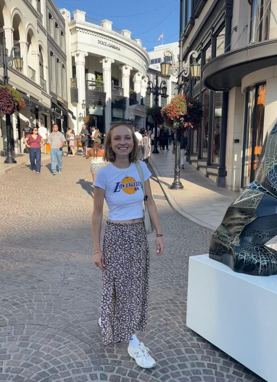 Carla Carla läuft auf einer geplasterten Straße. Im Hintergrund erkennt man viele kleine Geschäfte.