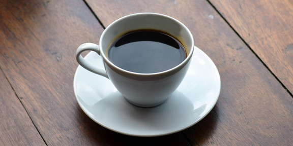 Tasse gefüllt mit Kaffee auf einem dunklen Holztisch.