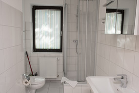 Ein Blick in das Badezimmer eines Apartments im Gästehaus. Man sieht die Dusche, die Toilette, das Waschbecken und den Spiegel.