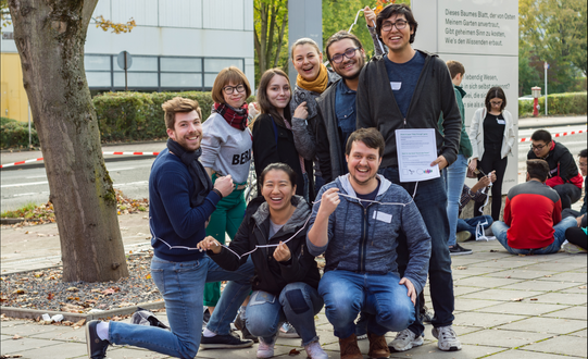 a group of international students in front of the International Meeting Center of the TU Dortmund University playing a game; in the background another group 