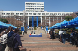 Man sieht ein großes Gebäude. Davor sind treffen und ein Slogan mit „ I <3 Sookmung“ steht als statue vor den Treppen die zum Gebäude führen. Rechts und links sieht man blaue Pavillons.