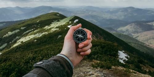 A hand is reacching out in front of the camera and holding a compass