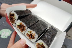 Hände halten eine Packung mit Sushi Rollen
