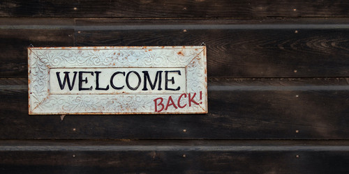 weißer "Welcome" Schild hängt am dunklen Holz. "Back" wurde handschriftlich hinzugefügt