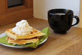 at the left two waffles with cream, at the right a black cup with coffee
