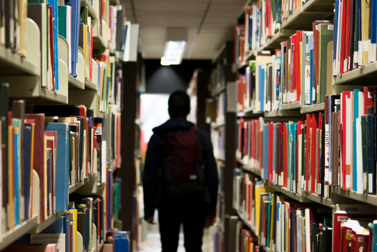 Ein männlicher Studierender steht in einer Bibliothek zwischen zwei Bücherregalen