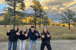 Gruppenfoto im Buffalo Park Hier sieht man drei Mädchen und einen Jungen, die alle in die Kamera lächeln. Im Hintergrund sind Bäume, die von der Sonne angestrahlt werden und gelb leuchten.