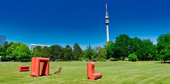 Florianturm vor blauem Hintergrund. Im Vordergrund grüne Wiese und Bäume.
