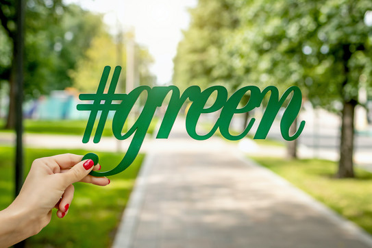 eine Person hält den Schriftzug "#green", mit einem Park im Hintergrund an einem sonnigen Tag