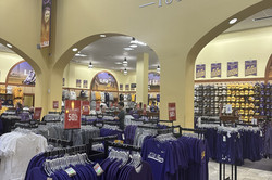 Hier sieht man den LSU Campus Shop. Man sieht zahlreiche Kleiderständer mit T-Shirts, Kappen und Pullis.