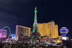 Las Vegas Blick auf Las Vegas mit vielen bunten, beleuchteten Gebäuden, einem Eifelturm, ein Riesenrad und Heisluftballon.