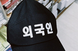 Eine schwarze Cappy, auf der weiße koreanische Schriftzeichen zu sehen sind. 
