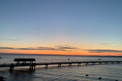 Hier sieht man einen Steg am Meer beim Sonnenuntergang. 