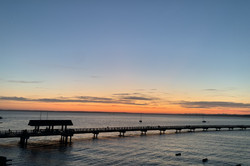 Hier sieht man einen Steg am Meer beim Sonnenuntergang.
