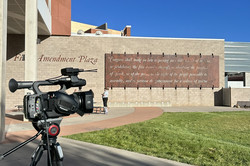 Filmdreh vor der School of Communication Hier sieht man eine Videokamera auf einem Stativ. Im Hintergrund ist eine Mauer mit einem großen Schriftzug zu sehen.