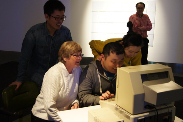 Eine Seniorin und vier Asiaten, die einen alten Computer bedienen