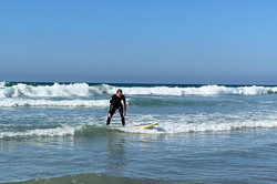 Eine Person auf einem Surfbrett in den Wellen des Meeres. Der Himmel ist blau. 