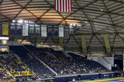 Eine große Halle mit vielen Menschen in gelb-blauen Uniformen auf einem Footballfeld und Menschen auf einer blauen Tribüne im Hintergrund. 