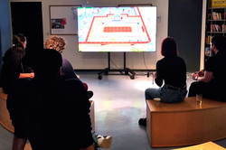 Menschen sitzen vor einem großen Bildschirm und spielen Videospiele.