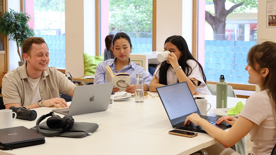 4 students eating waffles, drinking coffee and reading books together at a table.
