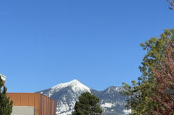 Verschneite Berge vor blauem Himmel, im Vordergrund ist ein braunes Gebäude und eine Straße zu sehen. 