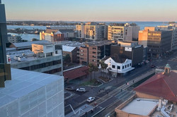 5:30pm in der Bib Das Bild zeigt die Aussicht von einem Gebäude auf eine belebte Gegend und dem Meer im Hintergrund.
