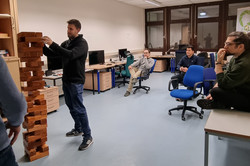 Ein Mensch steht neben einem großen Jenga-Turm. Weitere Menschen beobachten ihn.