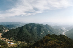Hier sieht man die Aussicht von einem Berggipfel mit dem Blick auf andere grüne Berge. 