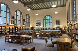 Bibliothek Man sieht zahlreiche Bücherregale und Holztische und -stühle.