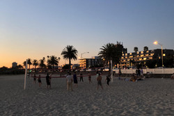 Hier sieht man eine Gruppe von Menschen am Strand Volleyball spielen beim Sonnenuntergang.