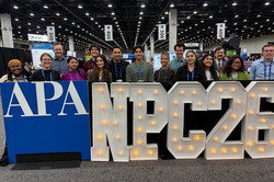 Man erkennt einige Studierende, die hinter einem großen Banner mit der Aufschrift "NPC26" in einer großen Halle stehen.