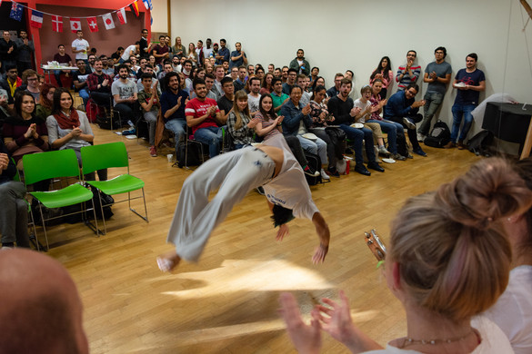 in the foreground a Capoeira dancer, in the background many international students watching and applauding