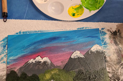 Hier sieht man eine selbst bemalte Leinwand. Man sieht Berge, die mit Schnee bedeckt sind.