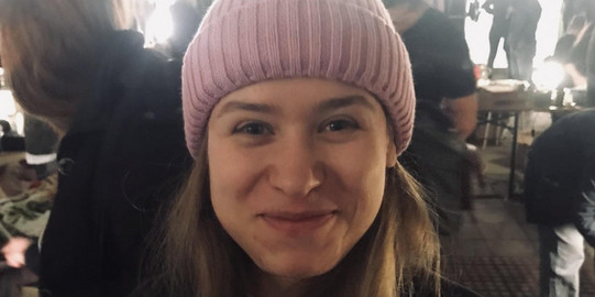 Hier sieht man die Studentin lächelnd mit einer Mütze auf dem Kopf. 