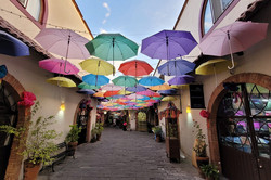 Gasse in Thlaquepaque Hier sieht man eine Gasse, über der zahlreiche bunte Regenschirme hängen.