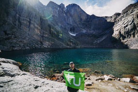 Zusehen ist Alessandro S. mit der TU Flagge in der Hand. Er befindet sich mitten in den Rocky Mountains.