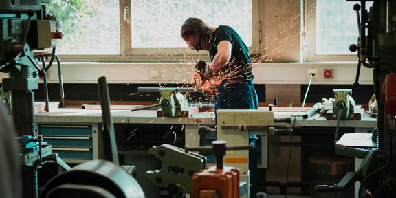 Ein Mann schweißt oder sägt und es fliegen Funken. 