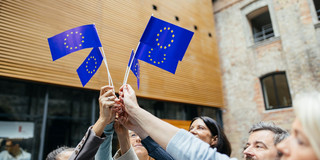 Menschen stehen in einem Kreis und halten kleine EU-Flaggen in der Luft.