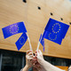 Menschen stehen in einem Kreis und halten kleine EU-Flaggen in der Luft.