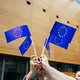EU Flaggen Menschen stehen in einem Kreis und halten kleine EU-Flaggen in der Luft.