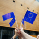 People standing in a circle and holding small EU flags up high