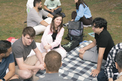 A group of participants are chatting on a picnic blanket in the park.