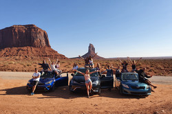 Eine Gruppe von Menschen posieren vor drei Autos für ein Foto.